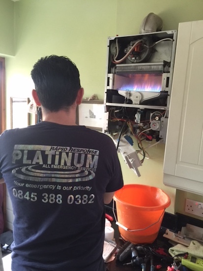 Emergency plumbing and heating engineer standing in front of a boiler carrying out fault finding test.