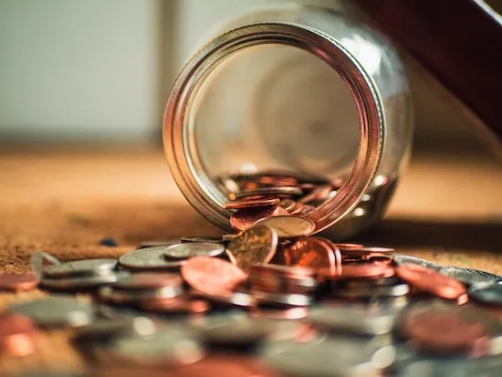 A jar of coins falling out onto a wooden table.